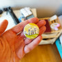 Childhood Days illustrated pin button held in hand for size reference.