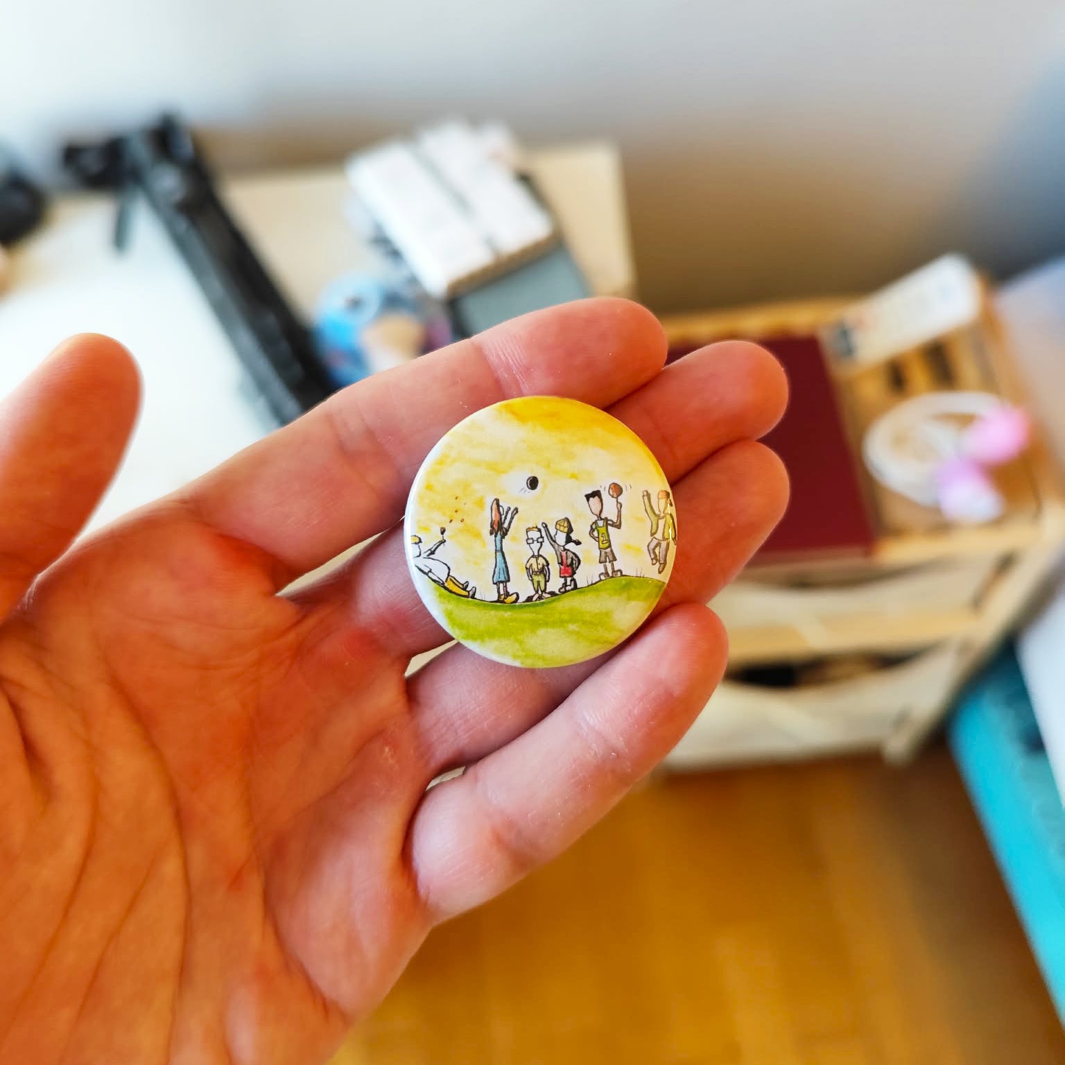 Childhood Days illustrated pin button held in hand for size reference.