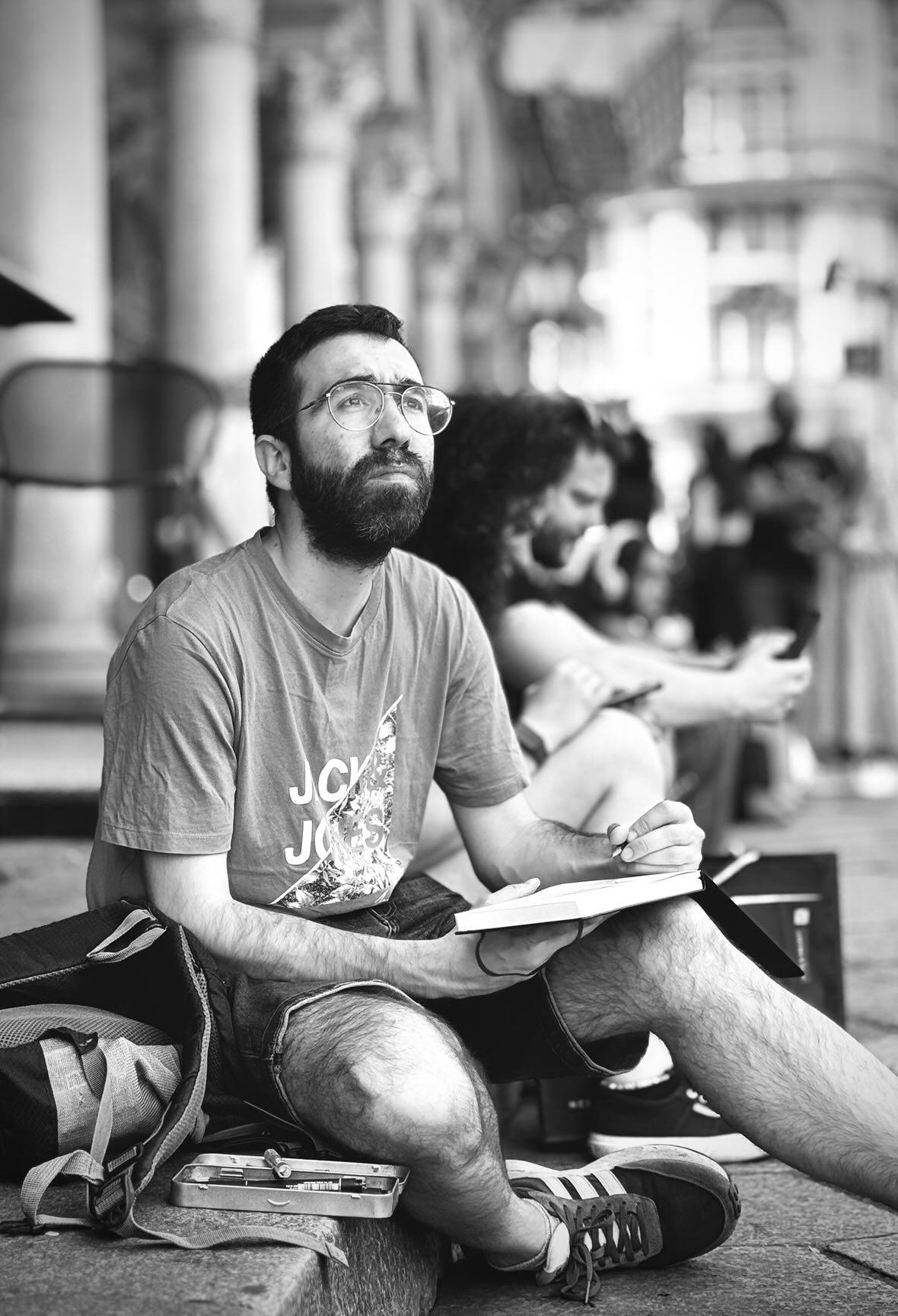 Black and white photo of illustrator Dimitris Kyrou sketching outdoors