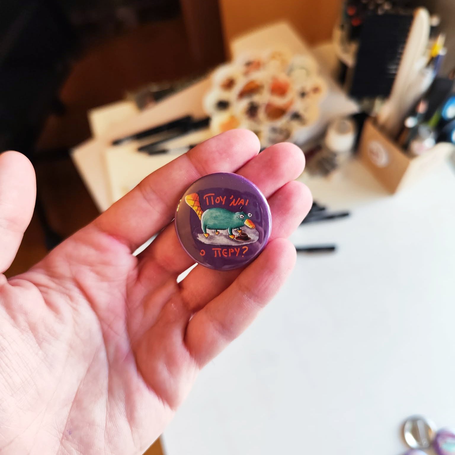 Exhausted Spy illustrated pin button held in hand for size reference.