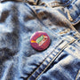 Exhausted Spy illustrated pin button attached to a denim jacket.