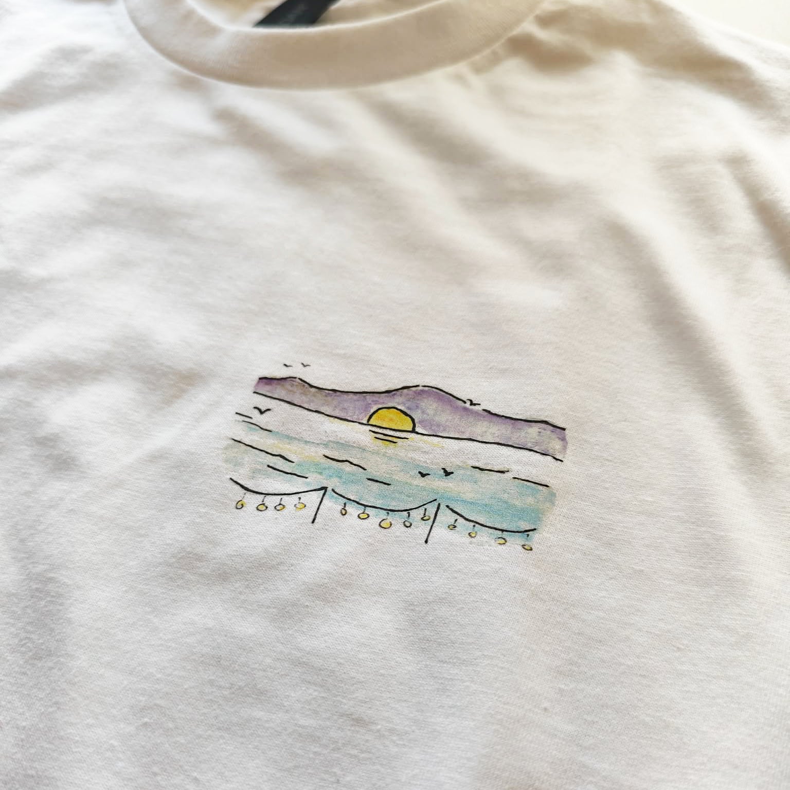 Close-up of the hand-drawn "Ikarian Dance" illustration printed on a white unisex t-shirt.