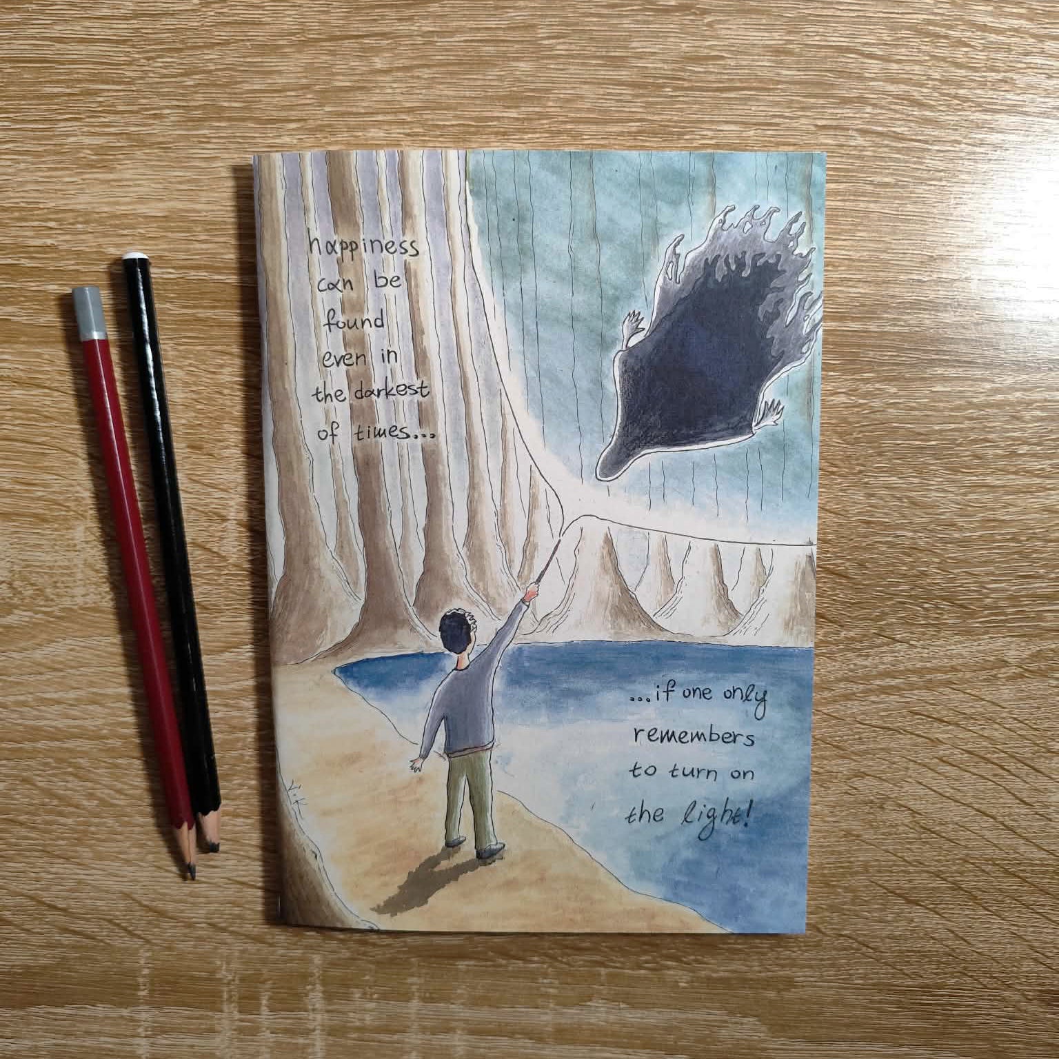 Light in the Darkness illustrated notebook displayed on a creative workspace.