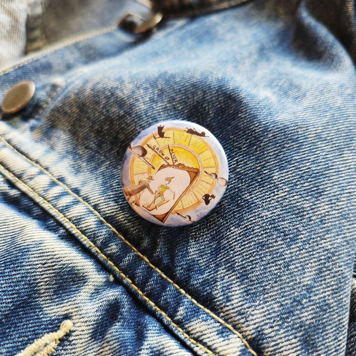 Never Grow Up illustrated pin button attached to a denim jacket.