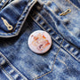 One Ship illustrated pin button attached to a denim jacket.