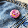 Sunset Dance illustrated pin button attached to a denim jacket.